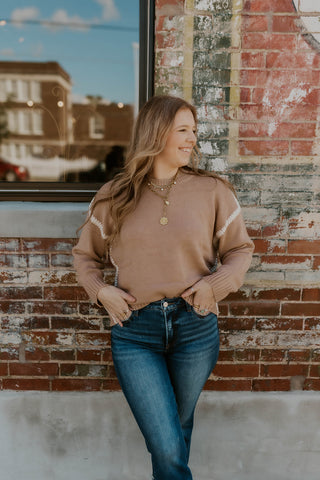 Model wearing taupe sweater with cream stitch detailing.